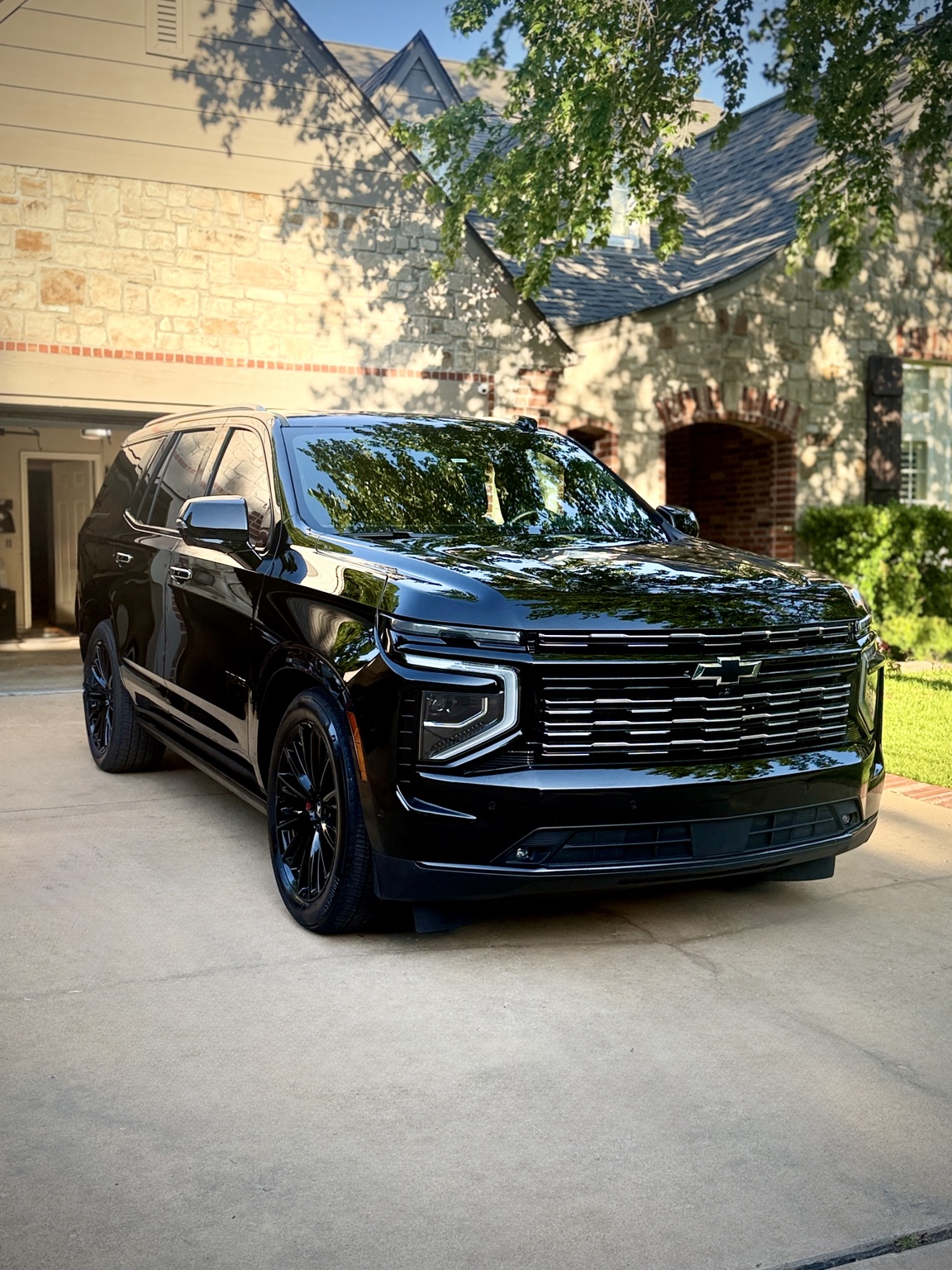 Glossy black Chevrolet SUV with black wheels, photographed on a driveway