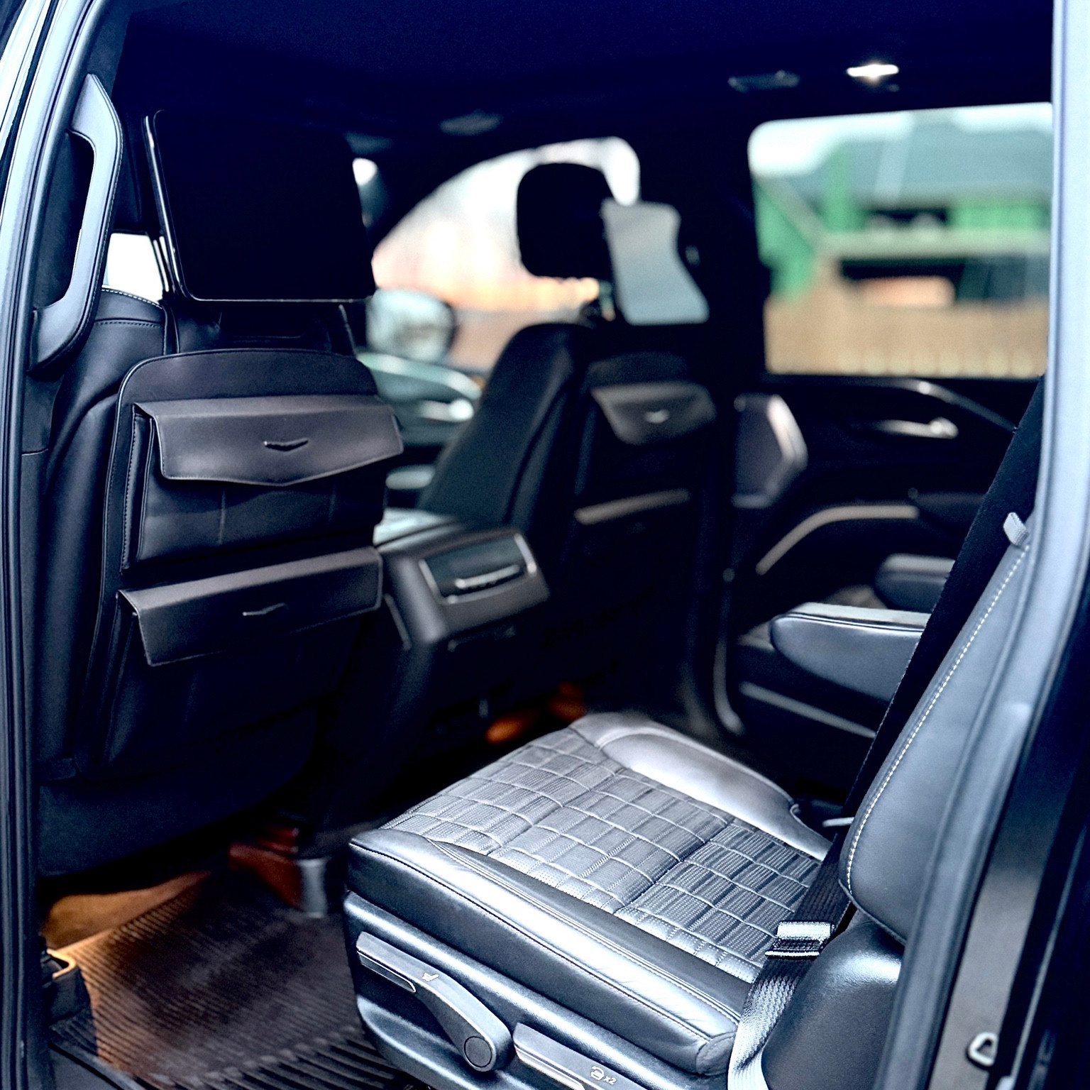 Quilted black rear captain’s chairs, seatback screens and floor mats in a Cadillac cabin