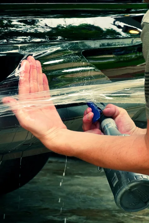 Hands smoothing protective film over glossy black paint