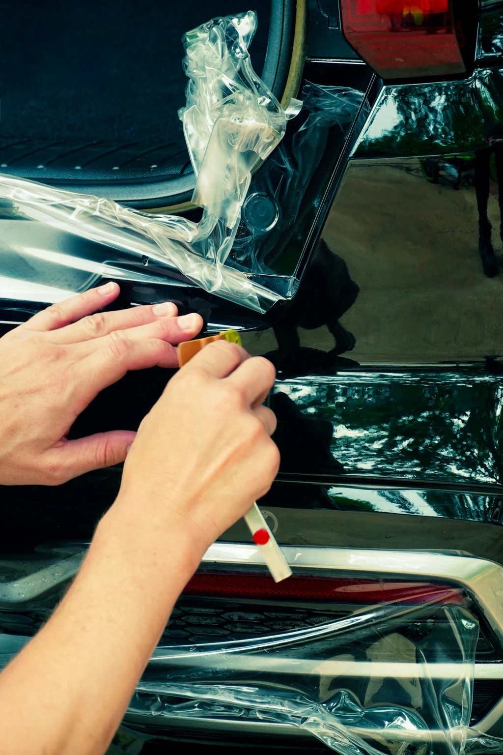 Hands trimming clear protective film around a rear light and bumper
