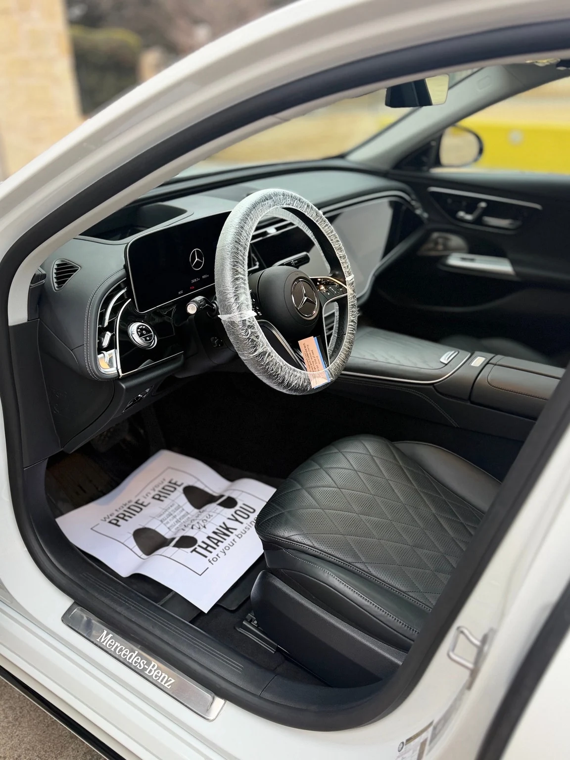 White Mercedes interior with a protected steering wheel, clean black leather seat and fresh paper floor mat