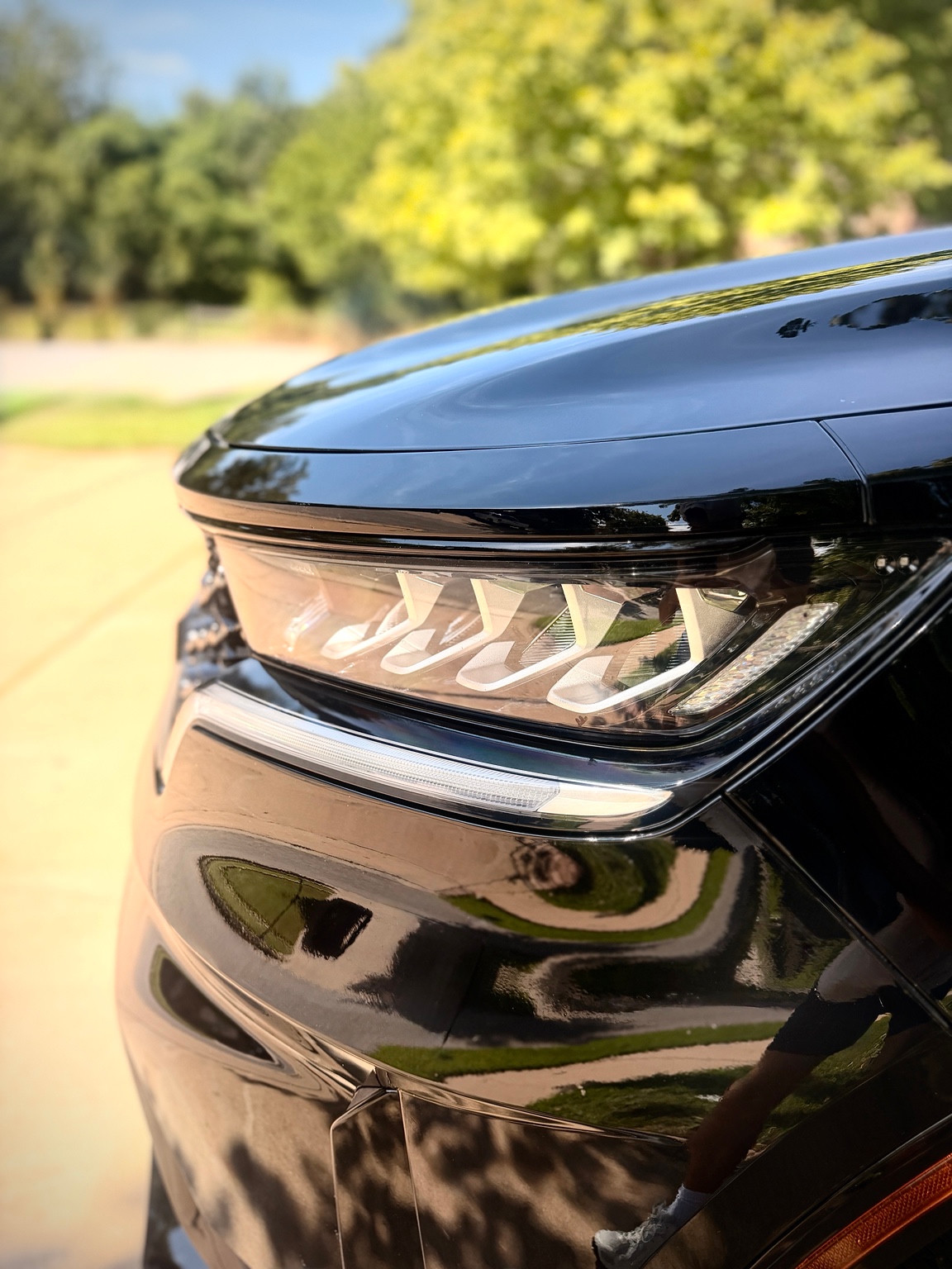 Close view of black paint and a headlight with natural reflections